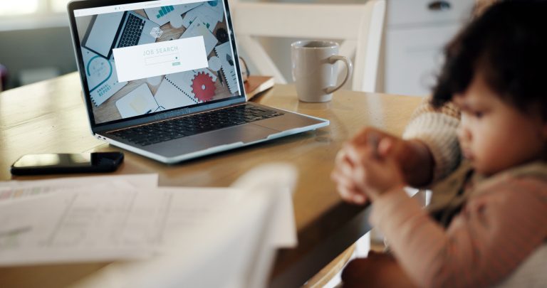 A photo of a person sitting at a computer with a small child in their lap.