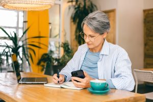 iäkkäämpi nainen kirjoittaa muistikirjaan