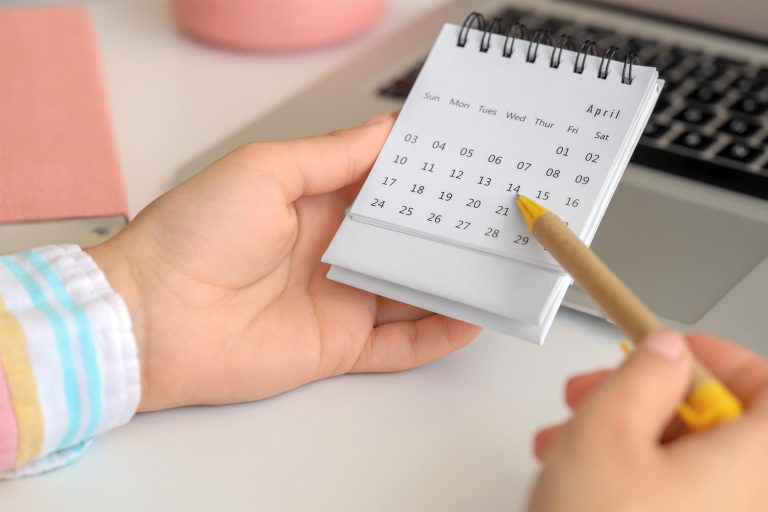 Kuvassa on kalenteri, johon henkilö on merkitsemässä kynällä. Vain henkilön kädet näkyvät.